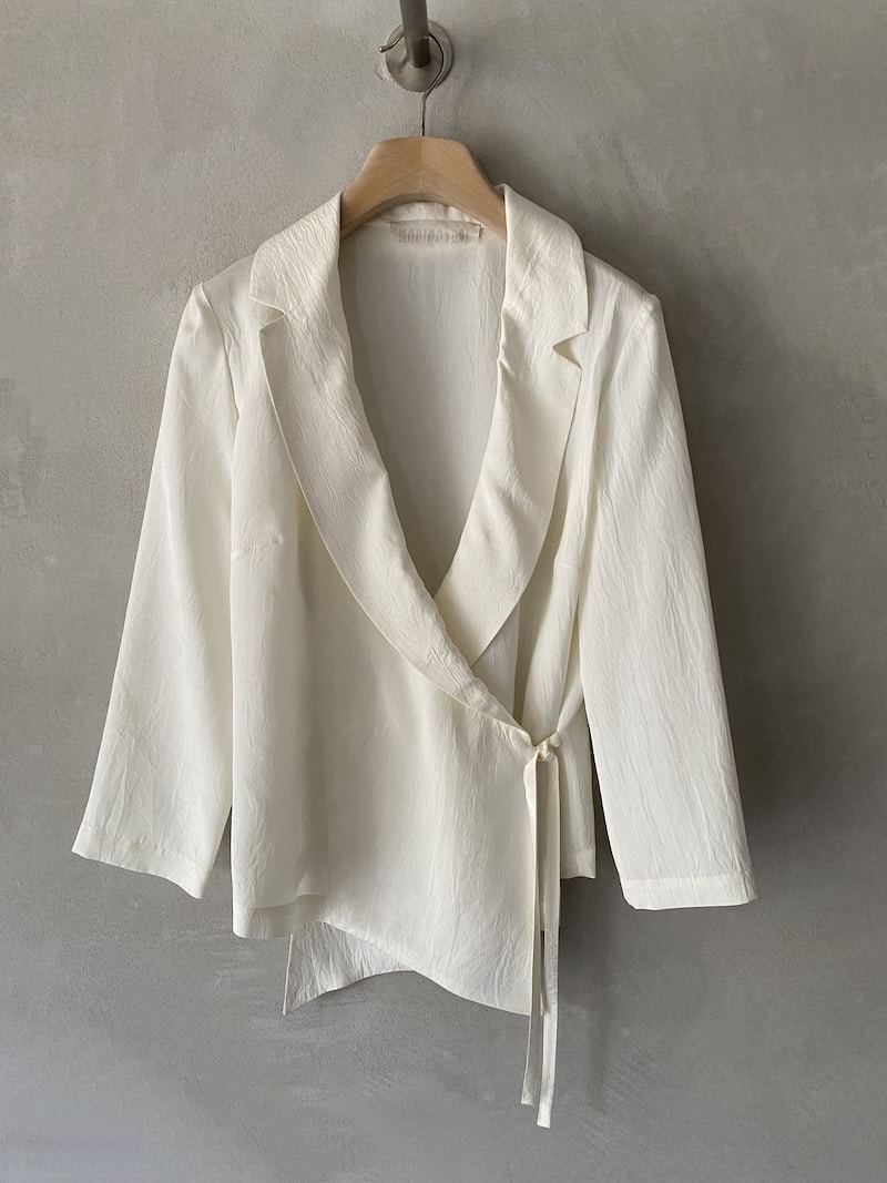 Giacca incrociata Marina Lari in acetato color bianco, con rever ampio, chiusura laterale con laccetto e fondo asimmetrico