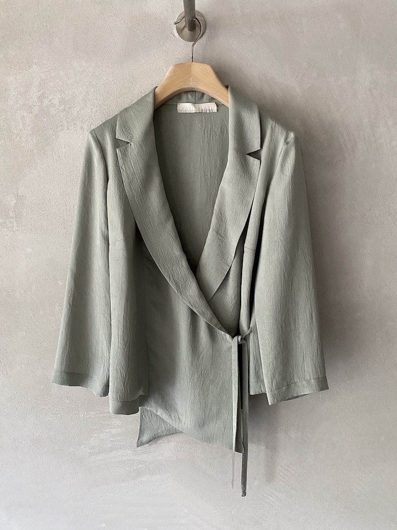 Giacca incrociata Marina Lari in acetato color salvia, con rever ampio, chiusura laterale con laccetto e fondo asimmetrico