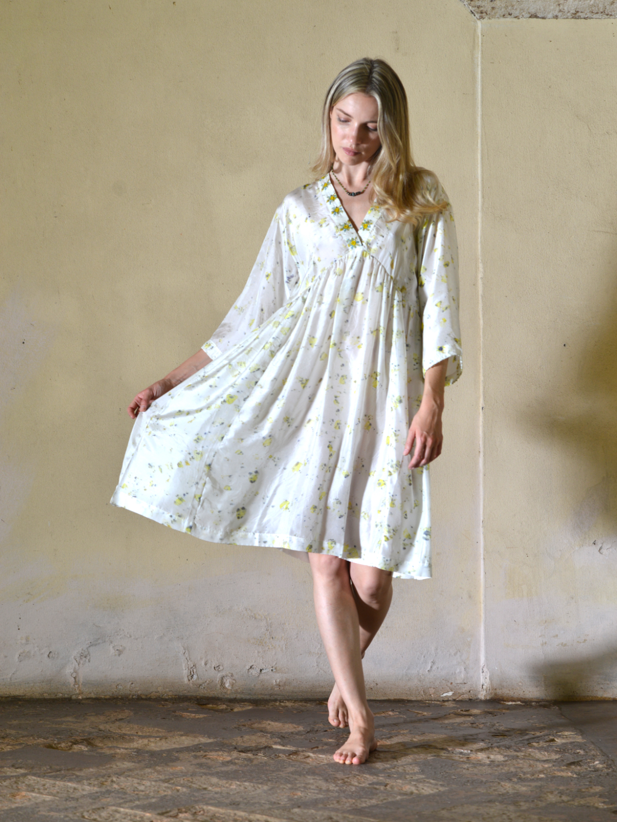 Abito bianco in seta habotai dipinta a mano, scollo a V con bordo ricamato, spalla scesa, manica lunga ampia a kimono, linea svasata con arricciatura sotto il seno, tasche laterali, lunghezza sopra il ginocchio, vestibilità morbida Nimbu