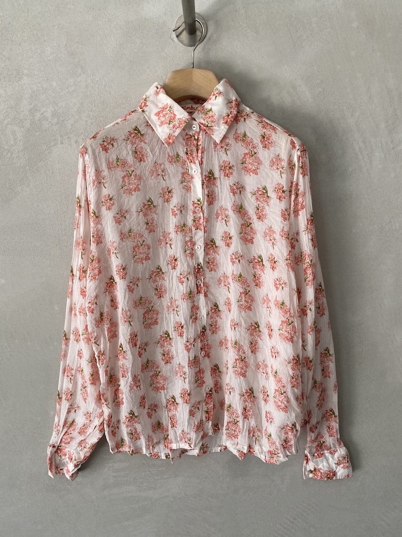 Camicia bianca in mussola di cotone con stampa floreale, texture leggermente stropicciata, colletto classico, maniche lunghe con polsino e bottone, apertura frontale con 7 bottoni, vestibilità over Nimbu