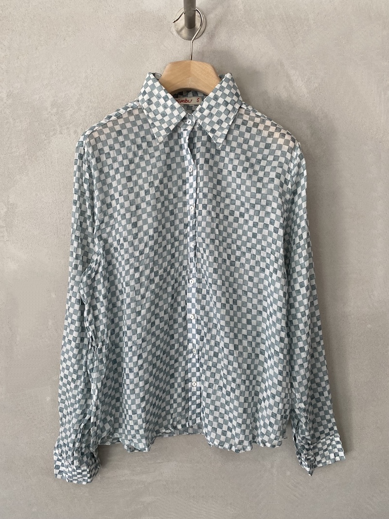 Camicia grigia in mussola di cotone con stampa a quadretti, texture leggermente stropicciata, colletto classico, maniche lunghe con polsino e bottone, apertura frontale con bottoni, vestibilità over Nimbu
